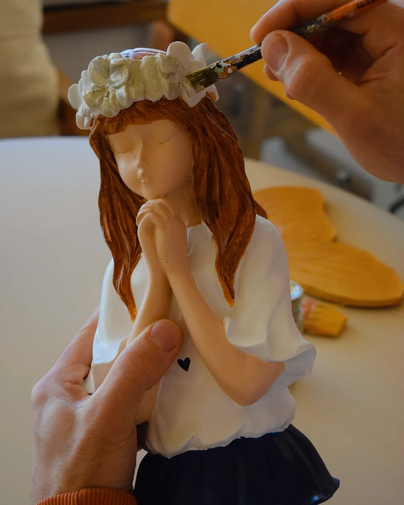 Una mano pintando con pincel una figura de yeso de una nena